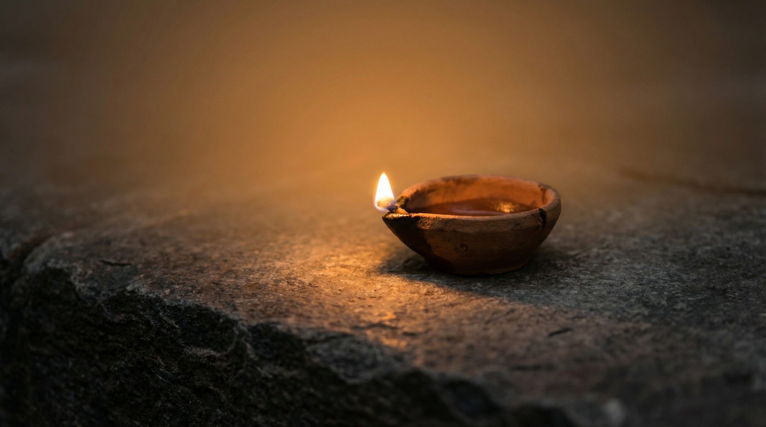 Ancient oil lamp burning with warm amber flame on plain stone surface