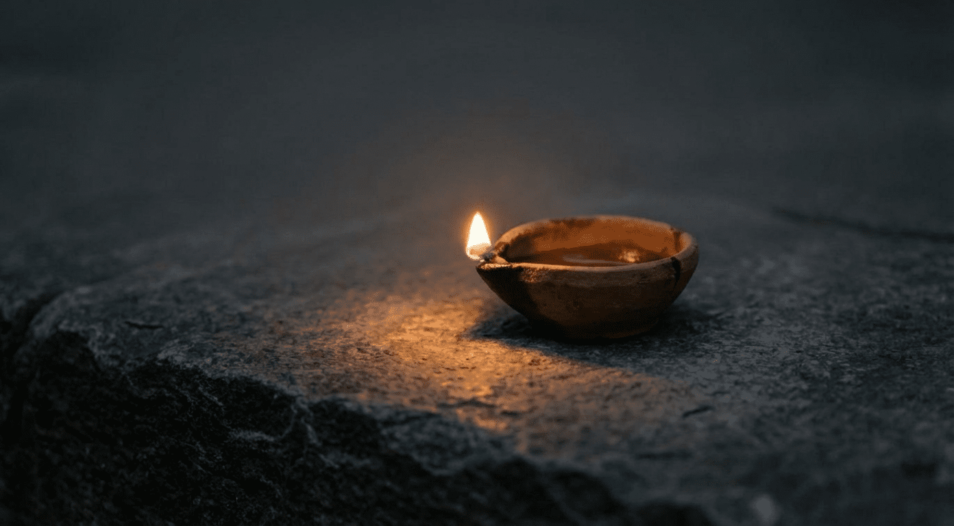 Small ancient oil lamp burning steadily on rough stone surface surrounded by darkness